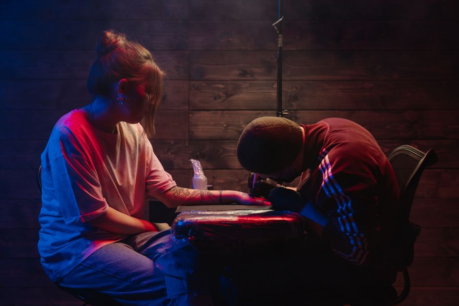 A tattoo artist works on a client's arm under neon lights, capturing the creative process.