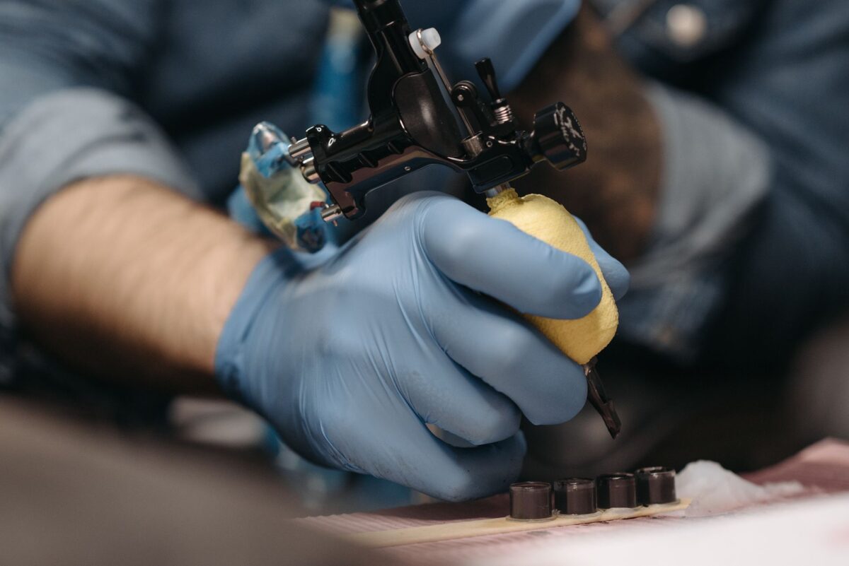 A tattoo artist working with a machine, gloved hands, close up