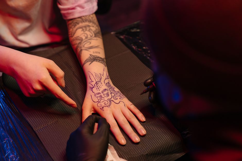 Tattoo artist crafting intricate dragon and nature design on a client's arm in studio.