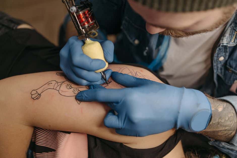 Tattoo artist using a machine to ink a client's arm with precision and skill in a studio setting.